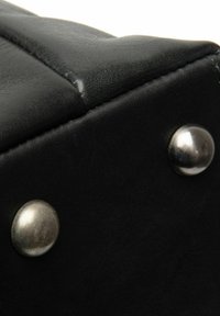 Oggetto in pelle nera con una superficie testurizzata, caratterizzato da cuciture visibili e due borchie metalliche arrotondate su un lato.