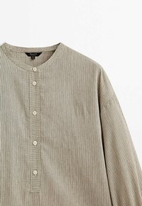 Chemise à manches longues beige et blanche à rayures verticales, avec un col officier et une patte de boutonnage verticale munie de cinq boutons blancs.