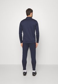 Marineblauwe sportoutfit met een langemouwen top en aansluitende broek. Glad, lichtgewicht materiaal met een zachte textuur, ontworpen voor comfort en bewegingsvrijheid.