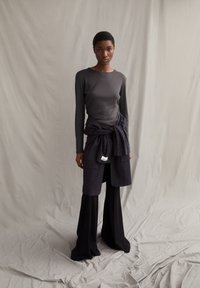 Langärmliges graues Oberteil, hoch taillierter gestreifter Wickelrock, weite schwarze Hose, einfarbige Farben, glatte Textur, minimalistisches Design.
