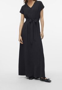 Svart, knälång klänning med V-ringning, korta ärmar och midjebälte. Har en texturerad tyg och faller ner till anklarna.