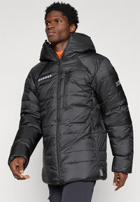 Casaco puffer preto com gola alta e capuz grande. Apresenta bolsos com fecho e uma textura acolchoada subtil. Logótipo refletor no peito e na manga.