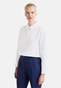 Camisa blanca de manga larga hecha de tela ligera con cuello abotonado, combinada con pantalones elásticos de cintura azul marino.