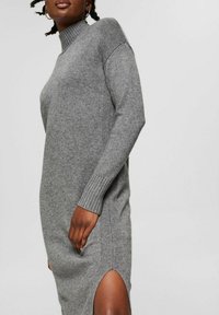 Robe en maille grise avec un col montant côtelé, une fente sur le côté et des détails côtelés sur les manches, offrant une coupe décontractée et moderne.