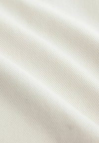 Detailný záber na hladkú, svetlobéžovú látku s jemnou diagonálnou žíhanou štruktúrou a mäkkými záhybmi vytvárajúcimi jemné tiene.