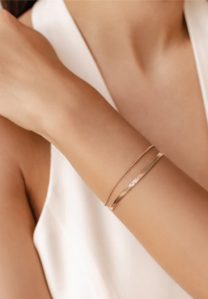 Gold-tone metal bracelets with textured and smooth finishes, one featuring small beads and the other a flat design, worn on a wrist.