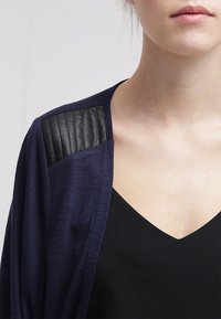 Námořnický kardigan s texturovanými černými akcenty na ramenech, měkká tkanina, otevřený přední díl a vršek s výstřihem do V. Detailní pohled na horní část těla.