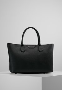 Czarna syntetyczna torebka o wyraźnej strukturze, z podwójnymi uchwytami u góry oraz logo marki na przedniej klapce. Gładka faktura z akcentami w rogach.