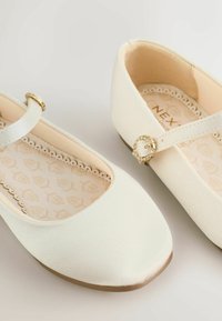 Balerini albi de balet prezintă un material superior texturat, formă rotundă a vârfului și o curea decorativă cu accente aurii. Căptușiți cu o branț cu model floral.