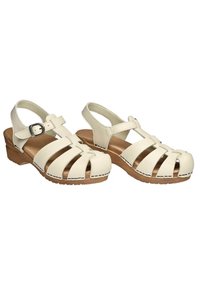 Sandali bianchi in pelle con punta chiusa, multiple fibbie, cinturino alla caviglia regolabile e tacco in legno. Cuciture decorative sui bordi.