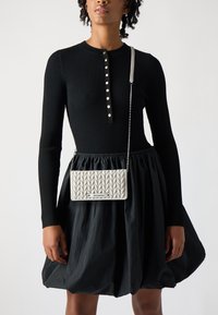 Top lungo a maniche ribattute nere con placca di bottoni e gonna nera svasata; borsa a tracolla argento con motivo trapuntato e tracolla a catena.
