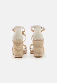 Beige espadrille sandals featuring a woven rope heel, back ankle strap, and open toe design with minimalistic leather accents.