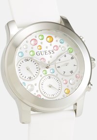 Guess klocka med silverfärgad boett, vit silikonsnodd, vit urtavla prydd med färgglada kristaller och tre subdials för datum och tid.