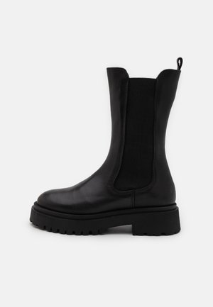 Bottines noires mi-mollet en cuir lisse avec des panneaux latéraux élastiques. Semelle en caoutchouc épaisse avec un motif de grip et une languette en tissu à l'arrière.