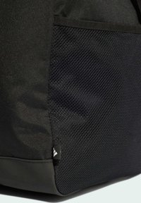 Black bag featuring a textured mesh side pocket, smooth fabric finish, and a small logo tag on the bottom corner.