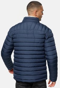 Navy puffer jacket with horizontal quilted design, high collar, and zip closure. Made of smooth, lightweight material, features elasticized cuffs.