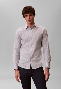 Chemise à rayures manches longues boutonnée, en gris clair et blanc, avec un col classique, une patte de boutonnage et une coupe ajustée.