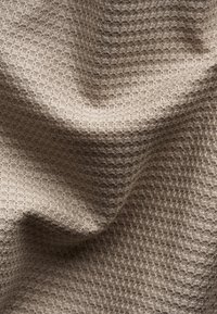 Tessuto beige testurizzato con un motivo a diamante, caratterizzato da una superficie morbida e tessuta che crea un'apparenza tridimensionale sottile.