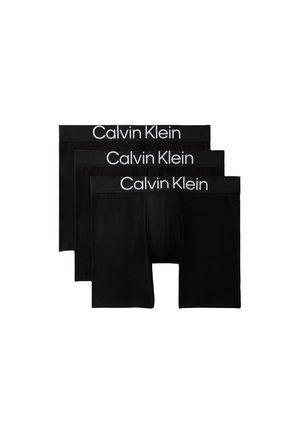 Trzy pary czarnych męskich bokserek z logo Calvin Klein na elastycznym pasie ułożone na białym tle.