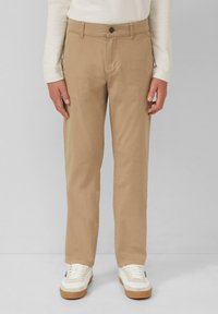 Beige katoenen chinos met een rechte snit, voorzakken en een knoopsluiting, gecombineerd met witte sneakers met tan accenten.