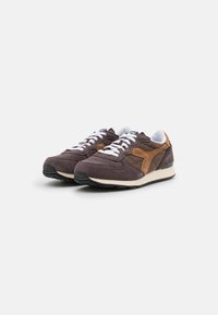Zapatillas de ante marrón con un acento beige, cordones blancos y una suela de goma negra. Parte superior texturizada con una puntera redondeada y un cuello acolchado.