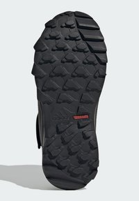 Black rubber outsole with aggressive tread patterns for traction. Features "adidas" and "TRAXION" branding in red near the heel.
