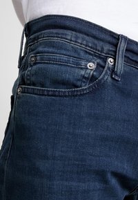 Mörkblå denimjeans med en slät yta, med en klassisk femfickorsdesign och silverfärgade metallaccenter fram.