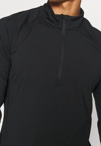 Schwarzes Zip-Up-Performance-Oberteil mit hohem Kragen, langen Ärmeln und Flachnaht für eine glatte Verarbeitung. Hergestellt aus leichtem, elastischem Material.