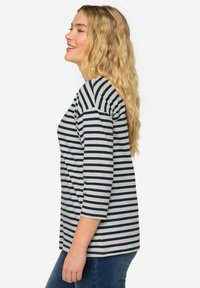Maglietta a maniche lunghe a righe in navy e grigio chiaro, caratterizzata da una vestibilità rilassata e colletto rotondo, abbinata a jeans in denim blu.