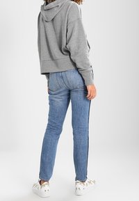Felpa grigia corta con cappuccio, abbinata a jeans skinny blu chiaro con strisce laterali e sneakers bianche con un design a motivi.