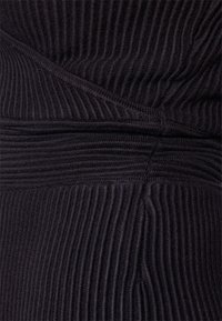 Tissu sombre texturé avec des nervures verticales, présentant un design croisé à la taille et des bords lisses, créant un aspect superposé.