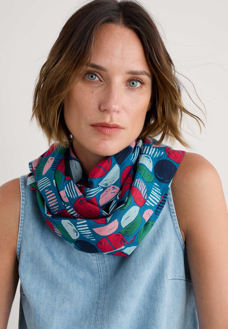 Mönstrad scarf med blå bakgrund som har abstrakta former i rött, grönt, rosa och vitt. Tillverkad av lätt tyg, arrangerad i en slinga.