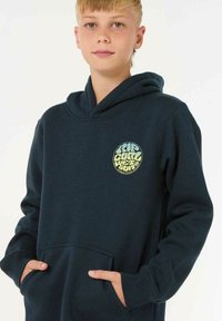 La sudadera con capucha de color azul marino cuenta con un bolsillo frontal, puños acanalados y un logo redondo con texto amarillo y verde en el pecho.