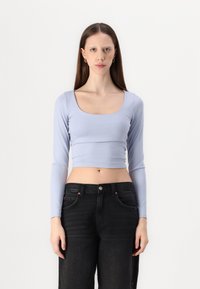 Lys blå langermet crop top med bred scoop hals, laget av et mykt, glatt stoff. Kombinert med høymidjede svarte jeans.