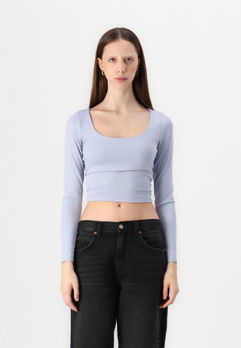 Lys blå langermet crop top med bred scoop hals, laget av et mykt, glatt stoff. Kombinert med høymidjede svarte jeans.