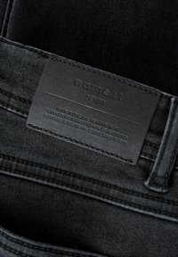 Crne traperice s ušivenim crnim kožnim ušicom s natpisom "name it DENIM" u blizini petlje za pojas.