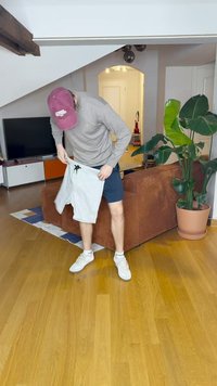 Gray shorts with a drawstring, being held by a person in a gray long-sleeve shirt and white sneakers, indoors on wooden floor.