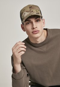 Kamouflage baseballpet met een iets platte rand, gecombineerd met een bruine sweatshirt met geribde mouwen en een ronde halslijn.