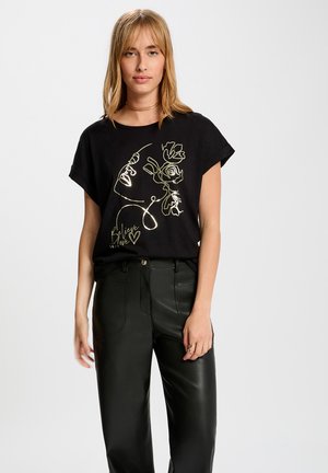 Camiseta negra de manga corta сon un diseño de arte lineal dorado de una cara con acentos florales y el texto "Cree en el amor."