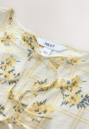Oberteil mit Blumenmuster, gelbe Blumen auf weißem kariertem Hintergrund. Mit einer Schlaufenbindedetail am Hals und einem Etikett mit der Aufschrift "NEXT".