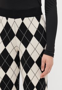 Zwart-witte gebreide broek met ruitpatroon, voorzien van een zwarte elastische tailleband, met een gestructureerde afwerking en diagonale ruitvormen.