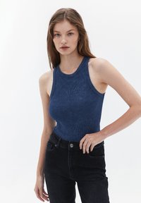 Marinblå ribbad tanktopp med rund halsringning, med breda axelband, i kombination med högmidjade svarta jeans. Slät textur.