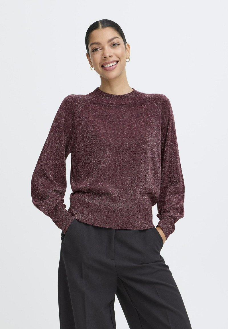 Pull bordeaux avec un effet métallique, col rond, manches longues et coupe décontractée. Associé à un pantalon noir à jambes larges.