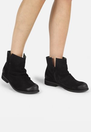 Black suede ankle boots with a slouchy design, rounded toe, side zipper, and flat wooden heel. Soft texture, minimal embellishments.