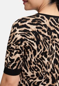 Bluzka w leoparda z prążkowaną teksturą, krótkimi rękawami, czarnymi akcentami i widokiem z tyłu, podkreślającym swobodny krój i wzór.