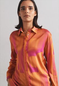 Silk skjorte med en blanding av oransje og rosa nyanser, med knappefront, lange ermer og spiss krage. Glatt tekstur, uten mønstre.