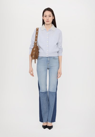 Cardigan azzurro in maglia a treccia con colletto bianco, abbinato a jeans a vita alta con pannelli laterali blu scuro e tacchi neri.