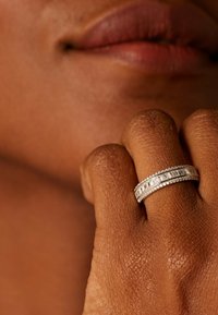 Twee zilveren ringen om een vinger, met rechthoekige en rond geslepen heldere stenen, tegen een gemarmerde huid.