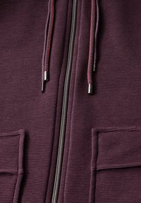 Purple zip-up hoodie with textured fabric, featuring two front pockets, silver zipper, and red-accented drawstrings.