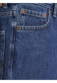 Primo piano di una tasca di jeans blu in denim con rivetti in rame e doppia cucitura visibile su tessuto strutturato.